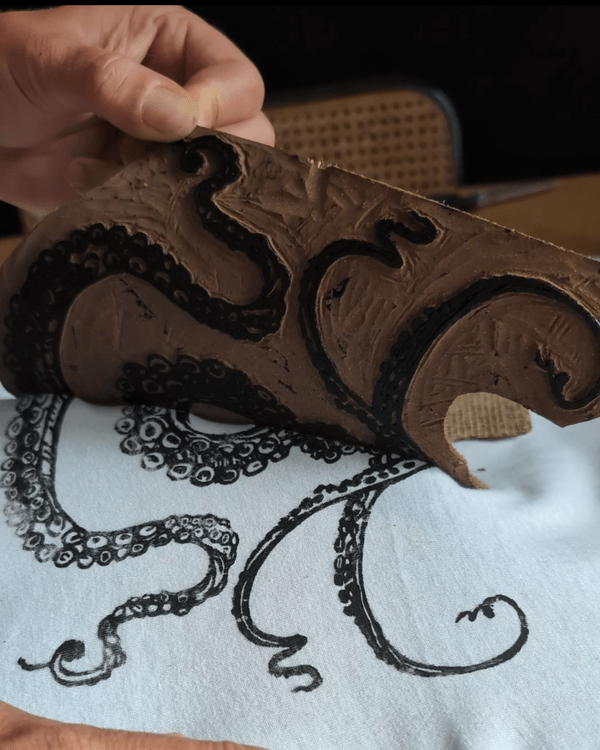 Retrait de la plaque de linogravure (encrée de noir) après l'impression réalisée au moyen d'une pression manuelle sur textile blanc.