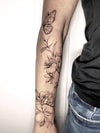Tatouage d'un papillon avec lys et fleurs diverses sur l'avant-bras